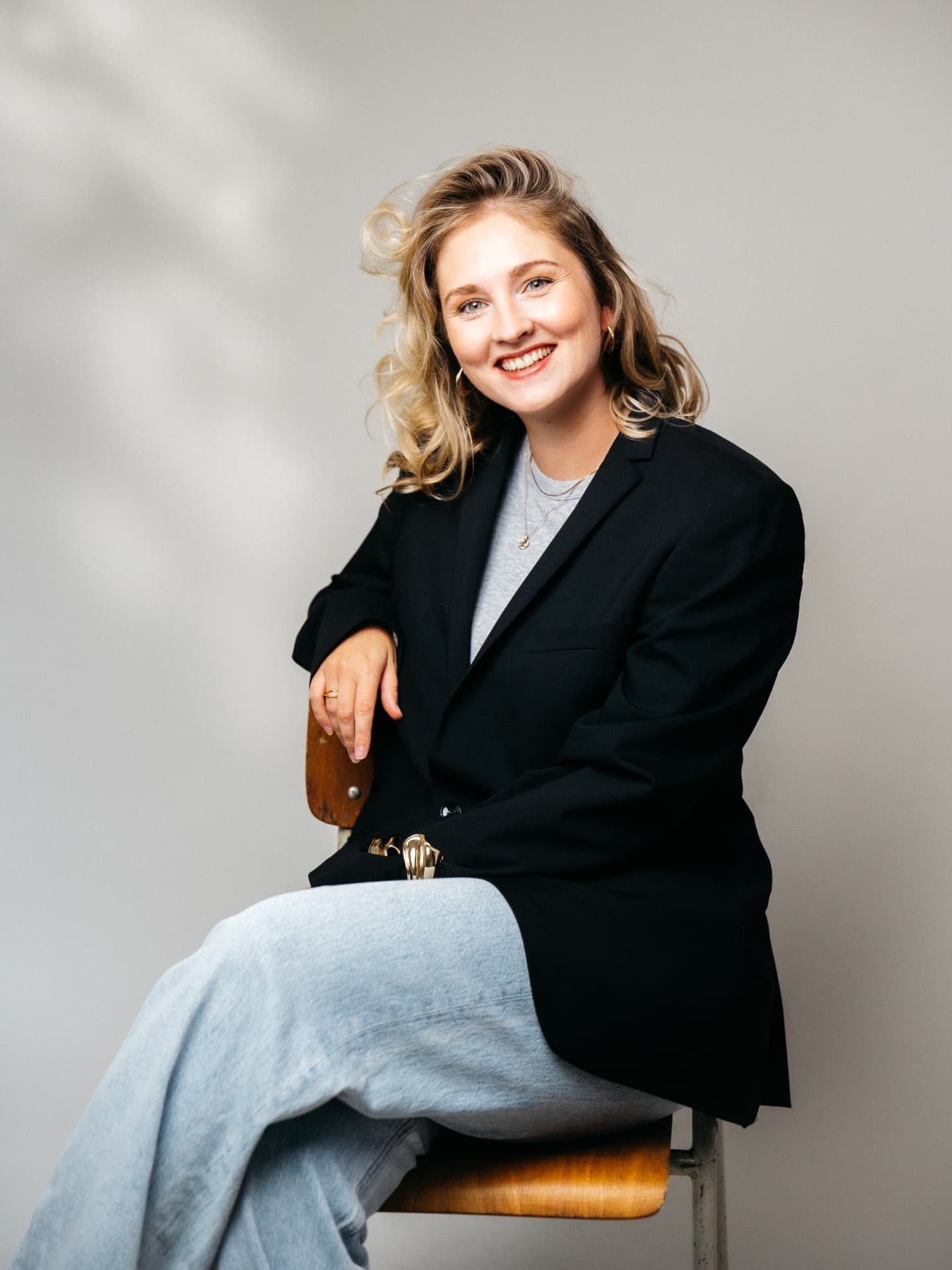 Kira Plagemann im schwarzen Blazer, lächelnd auf einem Stuhl